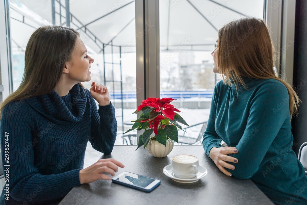 Two young women sitting in cafe and looking out the winter window Two young women sitting in cafe and looking out the winter window