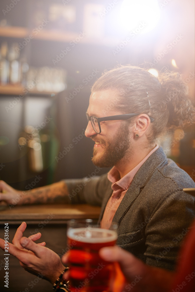 Handsome caucasian hipster leaning on bar counter and talking to his friend. Pub interior. Nightlife.