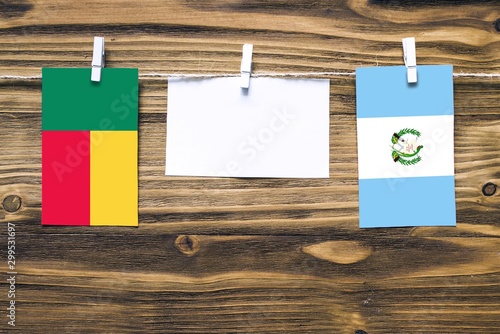 Hanging flags of Benin and Guatemala attached to rope with clothes pins with copy space on white note paper on wooden background.Diplomatic relations between countries.