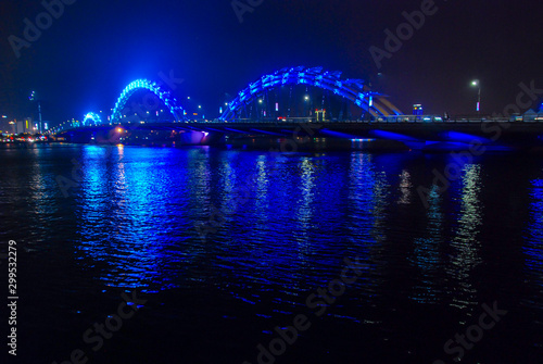 Blue illuminated Dragon Bridge in Da Nang at night reflected in Han river, Vietnam 