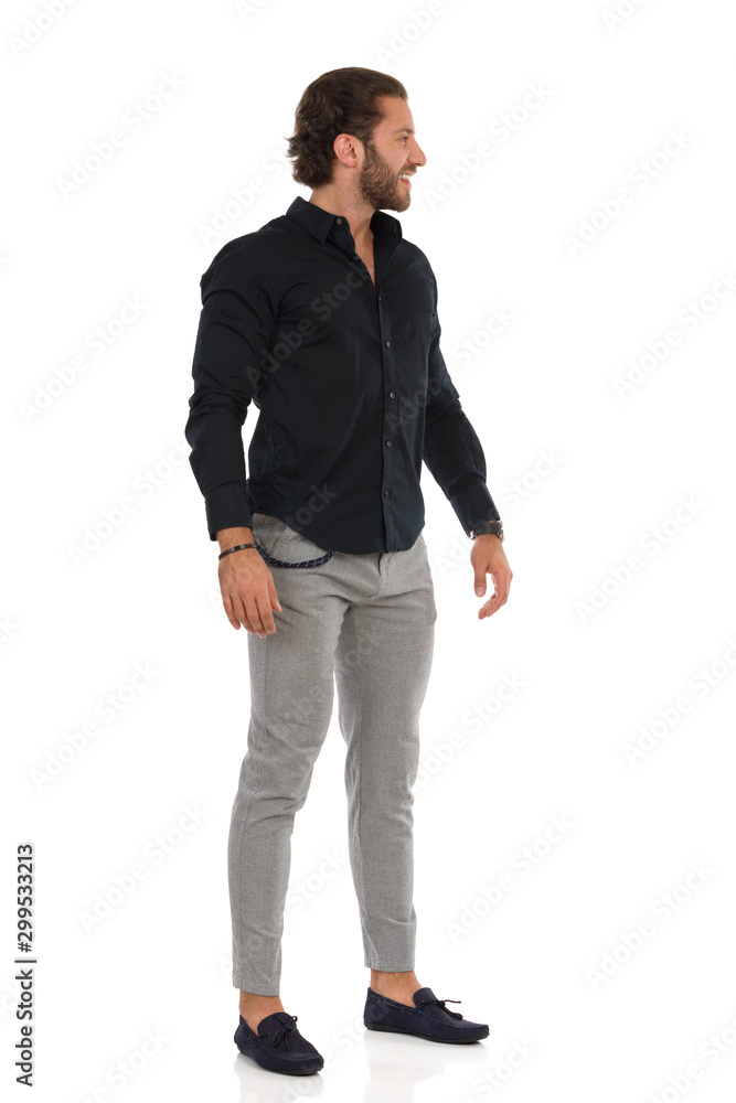 Handsome Man In Gray Trousers, Moccasins And Black Shirt Is Standing Relaxed And Looking Away Handsome Man In Gray Trousers, Moccasins And Black Shirt Is Standing Relaxed And Looking Away