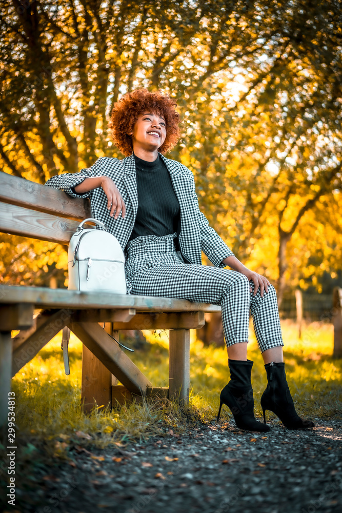 A smiling young Dominican woman sitting on a bench in autumn A smiling young Dominican woman sitting on a bench in autumn
