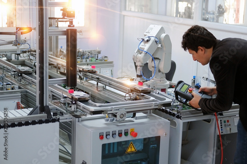 Man is holding teach panel to control a robotic arm which is integrated on smart factory production line. industry 4.0 automation line which is equipped with sensors and robotic arm. Selective Focus. photo