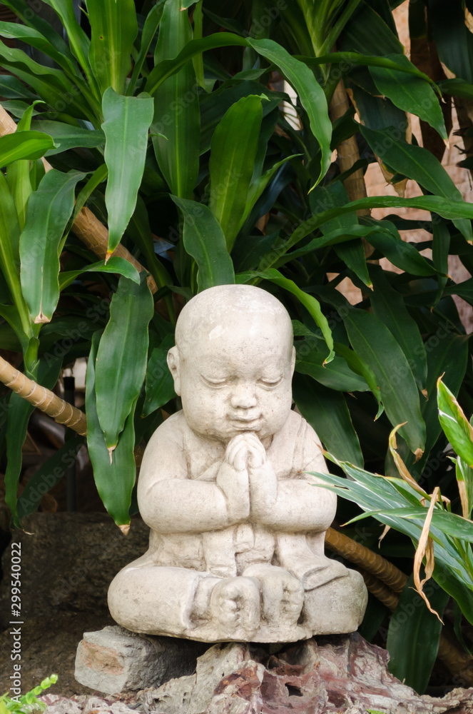 Cute little Buddha stone statue praying and smiling with eyes closed Cute little Buddha stone statue praying and smiling with eyes closed