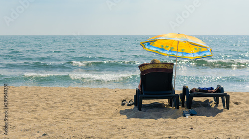 people on sunbeds under an umbrella relax on the beach against the sea