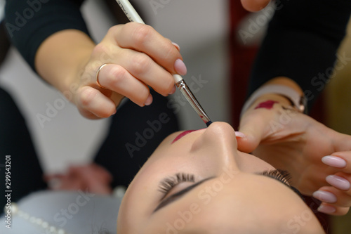 Studio photo of the work of a makeup artist by a hairdresser beautician. Creating beautiful makeup and hairstyles  rejuvenating the skin of the face. The professional is working with special tools.