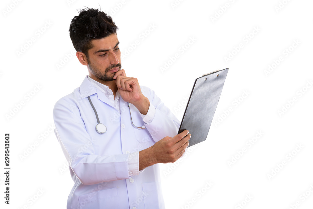 Portrait of young handsome bearded Persian man doctor holding clipboard Portrait of young handsome bearded Persian man doctor holding clipboard