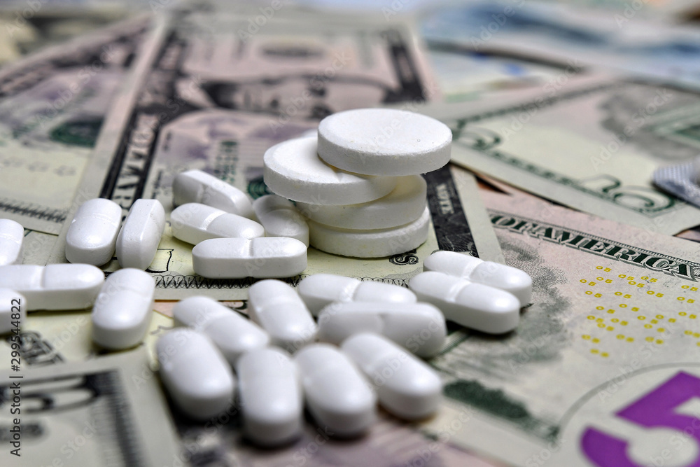 Pills on the background of the various national currency banknotes. The concept of medical availability and increasing medical expenses Pills on the background of the various national currency banknotes. The concept of medical availability and increasing medical expenses
