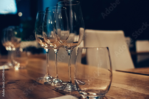 Empty glasses on wooden table, served for wine tasting event. Bar or shop interior, subdued light, lovely atmosphere. Selective focus. Film Grain effect. Low Key Image
