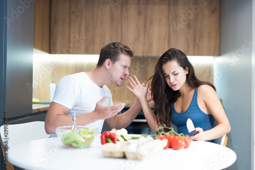 young couple having fight while cooking breakfast in the kitchen husband shouts loud at his wife family quarrel photo
