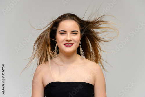 Studio large photo portrait of a beautiful girl with long beautiful flowing hair and excellent make-up on a gray background in different poses. She smiles.