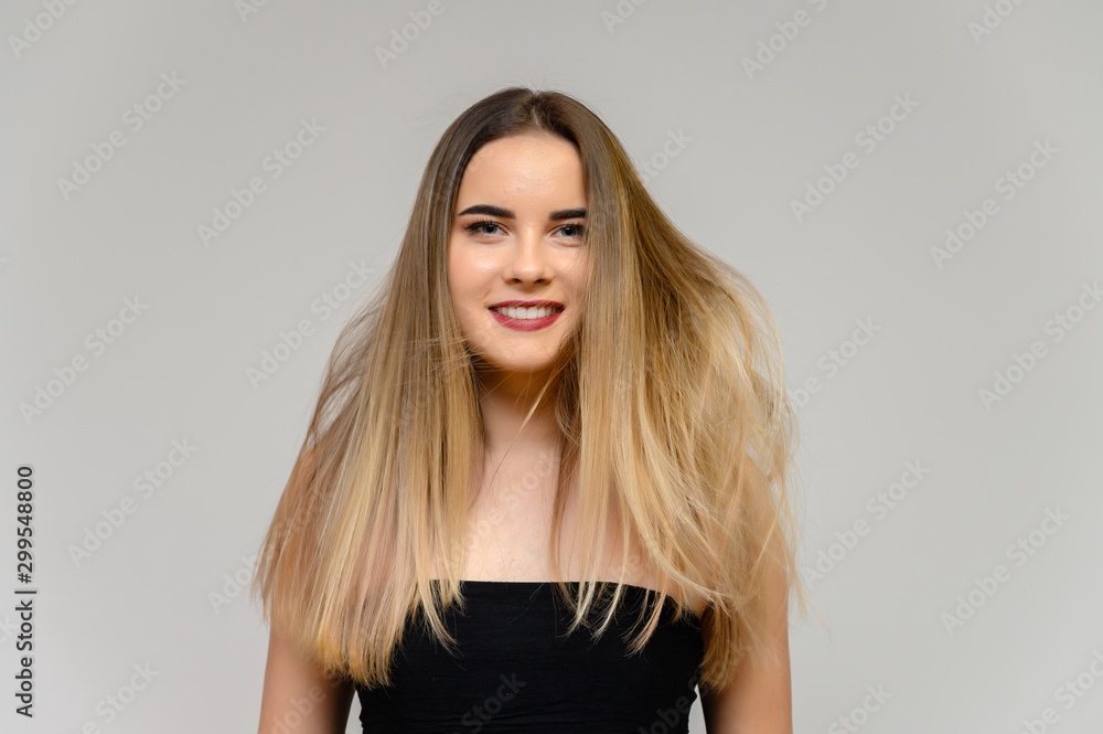 Studio large photo portrait of a beautiful girl with long beautiful flowing hair and excellent make-up on a gray background in different poses. She smiles. Studio large photo portrait of a beautiful girl with long beautiful flowing hair and excellent make-up on a gray background in different poses. She smiles.