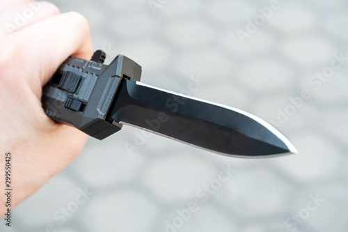 Closeup view of a hand with a black pocket folding knife blade facing forward. Selective focus