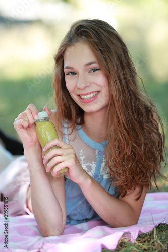 Jeune fille dégustant un smoothie allongée dans l'herbe en été