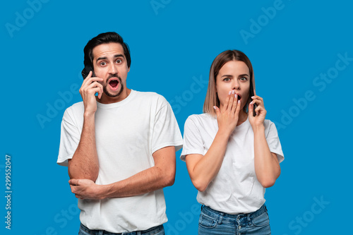 Blond woman and brunet man in white tees and blue jeans are surprised talking on the phone.