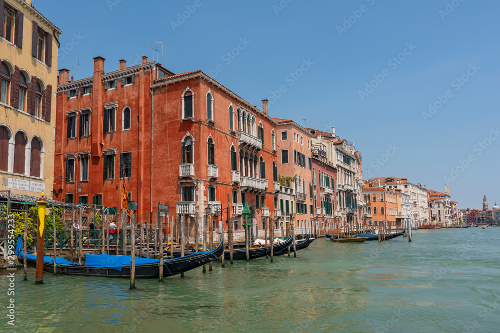 Row of brightly colored Gothic buildings on The Grand Canal with a row of docked blue Gondolas, Venice, Italy.