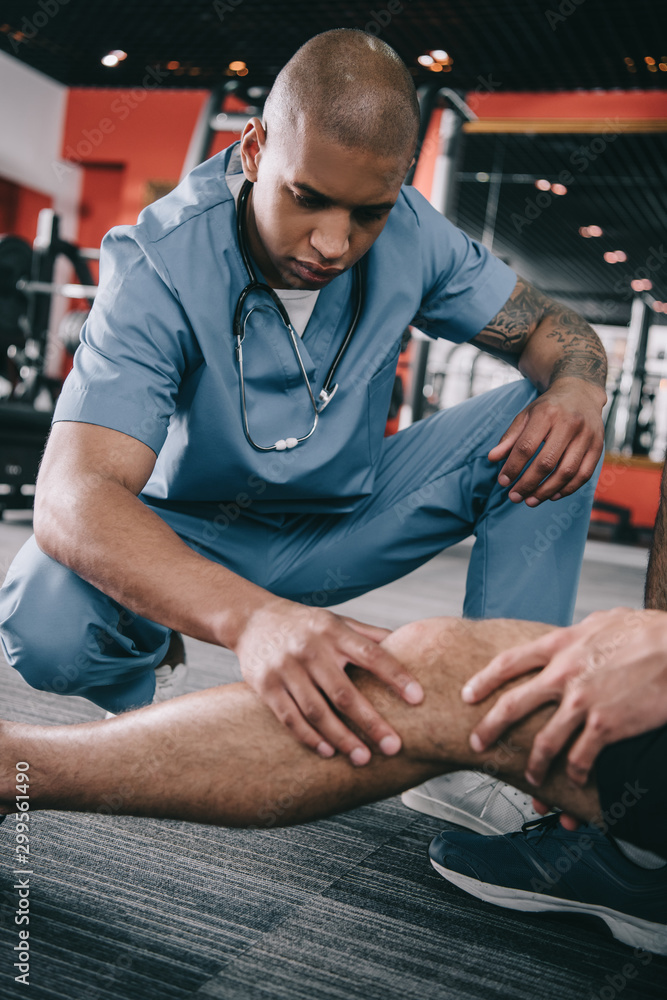 serious african american doctor examining injured knee of sportsman