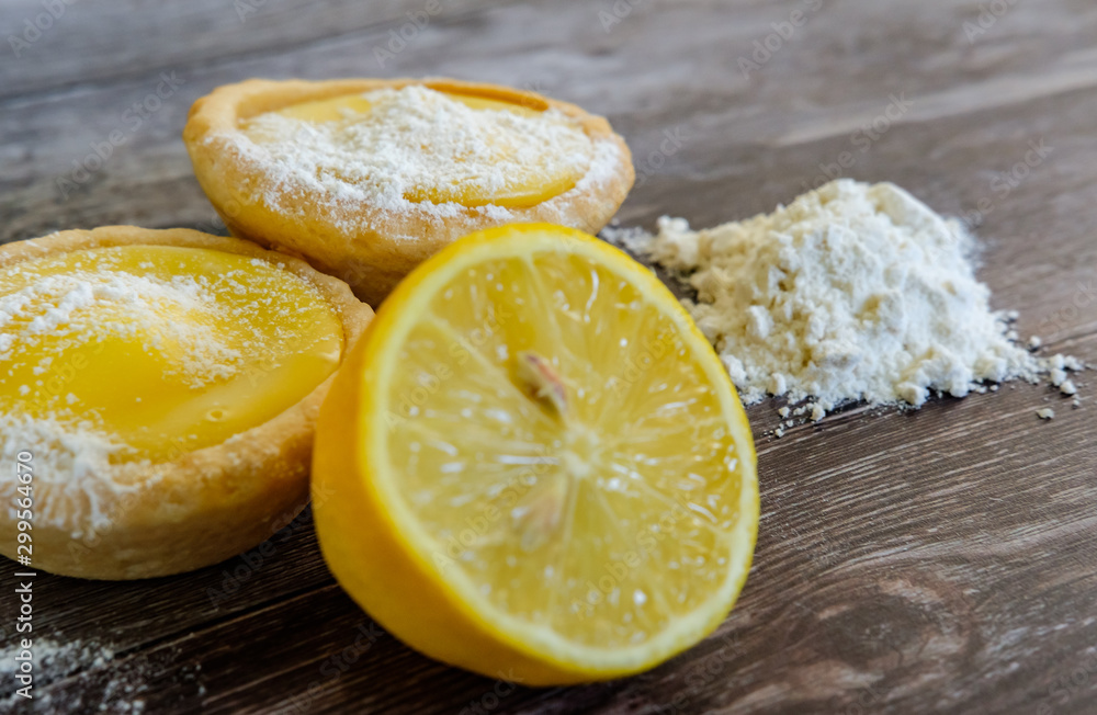 Close-up view of freshly made lemon cakes shown on a traditional wooden table together with a sliced lemon and baking flour used in the bakin Close-up view of freshly made lemon cakes shown on a traditional wooden table together with a sliced lemon and baking flour used in the bakin