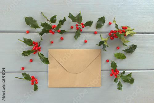 Christmas holly Ilex aquifolium isolated on blue table background. Evergreen leaves with red berries. Decorative floral frame  web banner. Flat lay  top view. Empty space for holiday text.