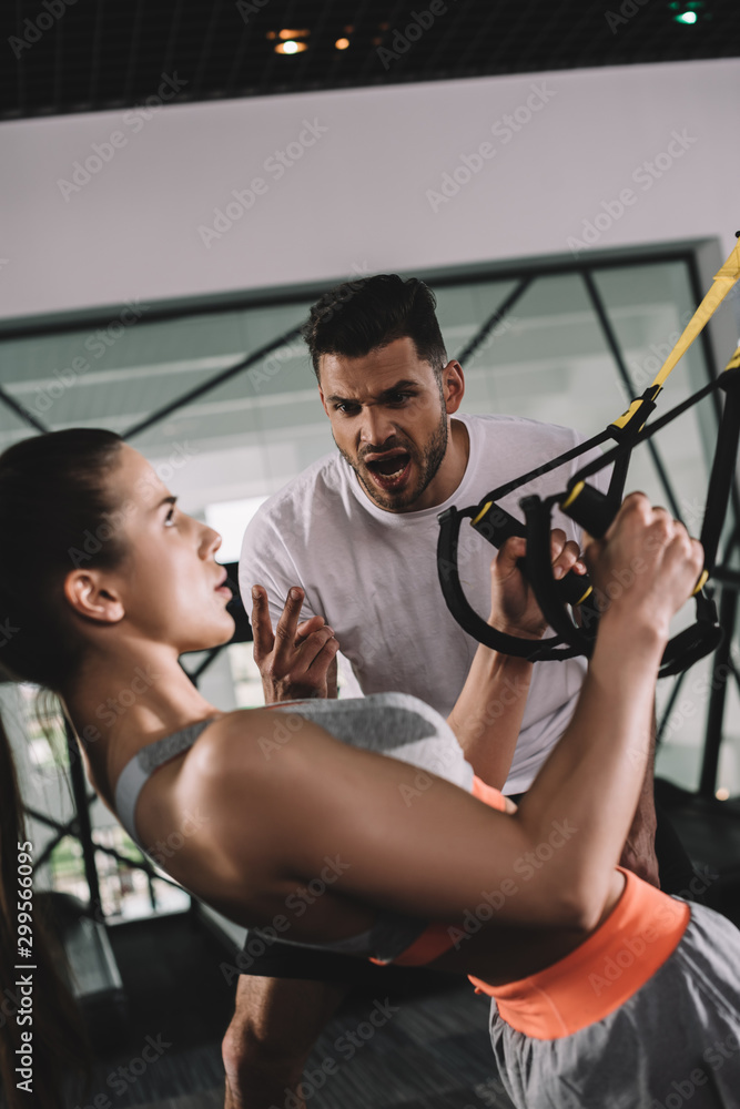 excited trainer shouting while motivating young sportswoman pulling up on suspension trainer excited trainer shouting while motivating young sportswoman pulling up on suspension trainer