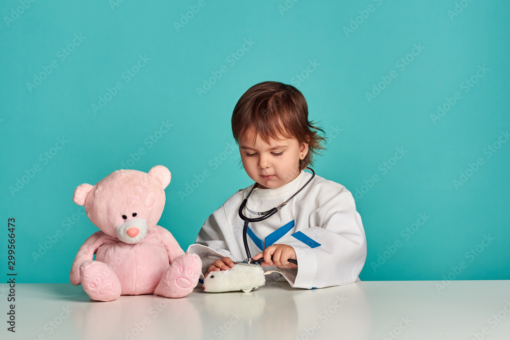 Smiling little girl in medical uniform play with stethoscope and teddy bear. Studio shot Smiling little girl in medical uniform play with stethoscope and teddy bear. Studio shot