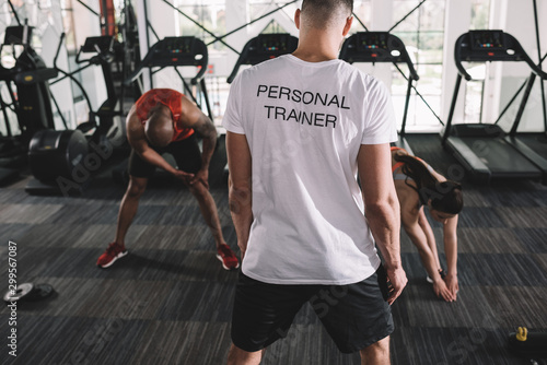 back view of personal trainer supervising multicultural athletes stretching in gym