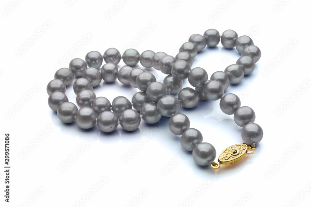 A single strand necklace of grey pearls with a gold clasp are crossed over itself. Shown on a white background with shadow. A single strand necklace of grey pearls with a gold clasp are crossed over itself. Shown on a white background with shadow.