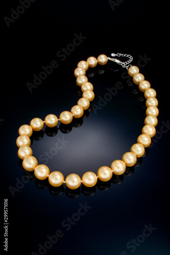 A single strand golden color pearl necklace sits on a black refective background.