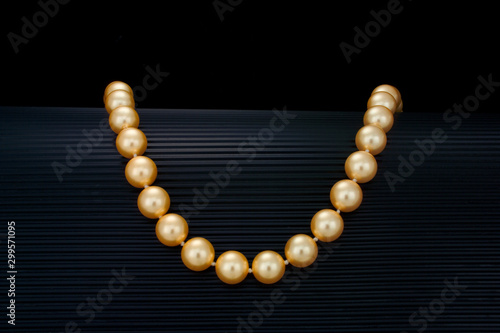 A single strand golden color pearl necklace drapes over a curve black ribbed background.