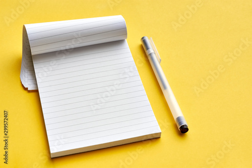 Top view of blank open notebook page with lines and transparent minimalistic fineliner pen on yellow background with copy space. For use as mock up.    
