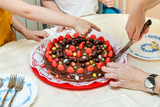 Mother is cutting a birthday cake at a kids party. Children's chocolate cake decorated with colorful candy.