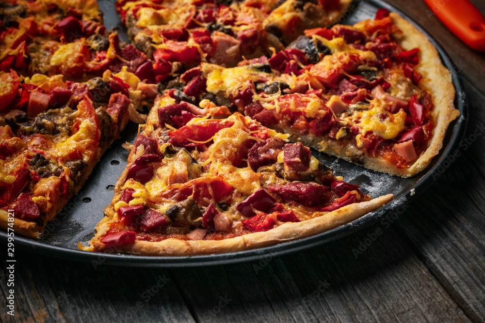 Closeup pizza with salami, sweet pepper, tomatoes, cheese and tomatoes in a metal dish on a wooden table Closeup pizza with salami, sweet pepper, tomatoes, cheese and tomatoes in a metal dish on a wooden table