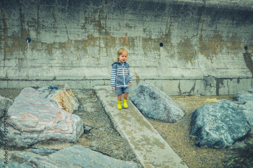 Little toddler running and playing on a rocky beach in the rain © LoloStock