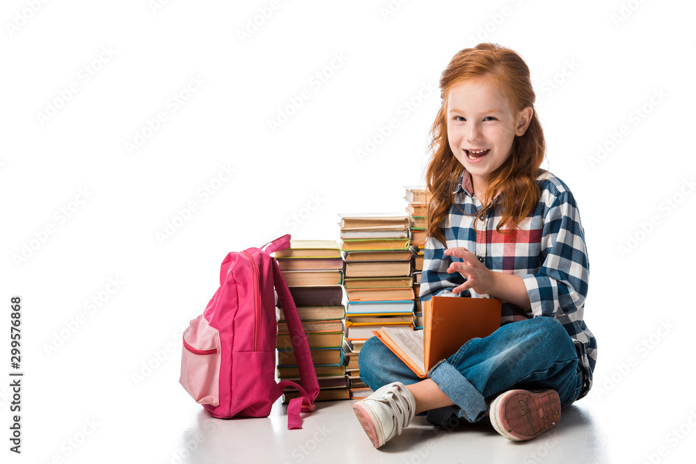cheerful redhead schoolkid sitting near books and pink backpack on white cheerful redhead schoolkid sitting near books and pink backpack on white