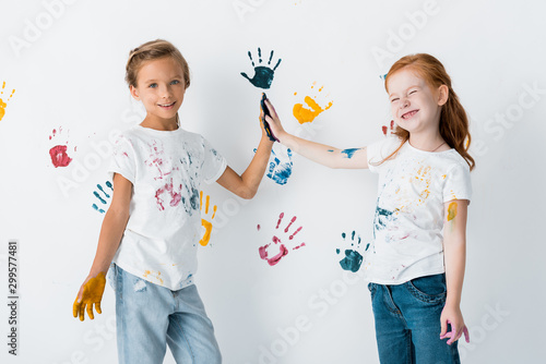 cheerful kids giving high five near hand prints on white