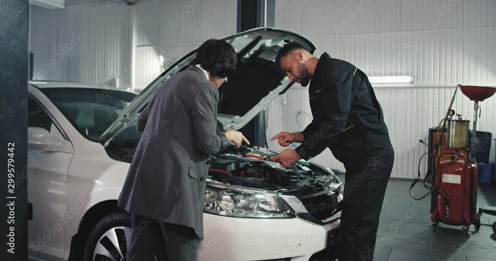 Auto garage mechanic man and a young woman engineer analyzing the problem of the engine they have a friendly conversation Auto garage mechanic man and a young woman engineer analyzing the problem of the engine they have a friendly conversation