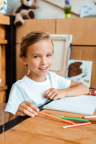 selective focus of positive kid smiling and looking at camera in art school