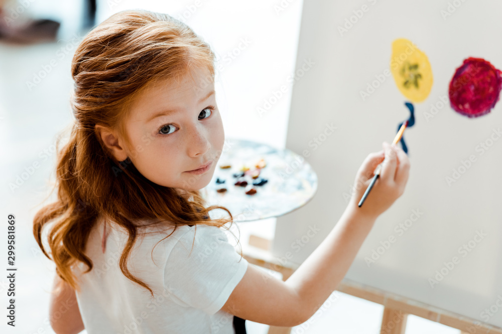 selective focus of cute redhead kid painting in art school - obrazy, fototapety, plakaty 
