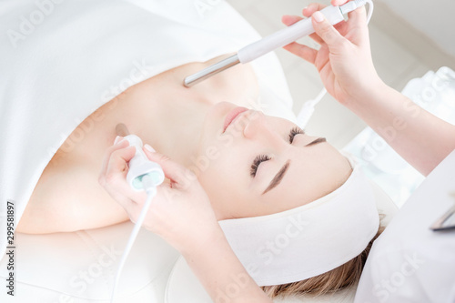 Beautician makes a microcurrent massage of face of girl client with help of modern salon equipment. The concept of hardware cosmetology. Cosmetic anti-aging procedure in clinic, facial skin care