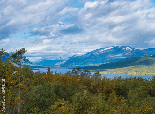 landscape with beautiful river Lulealven, snow capped mountain, birch tree and footpath of Kungsleden hiking trail near Saltoluokta, north of Sweden, Lapland wild nature. Summer blue sky photo