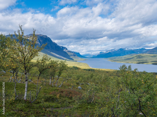 landscape with beautiful river Lulealven, snow capped mountain, birch tree and footpath of Kungsleden hiking trail near Saltoluokta, north of Sweden, Lapland wild nature. Summer blue sky photo