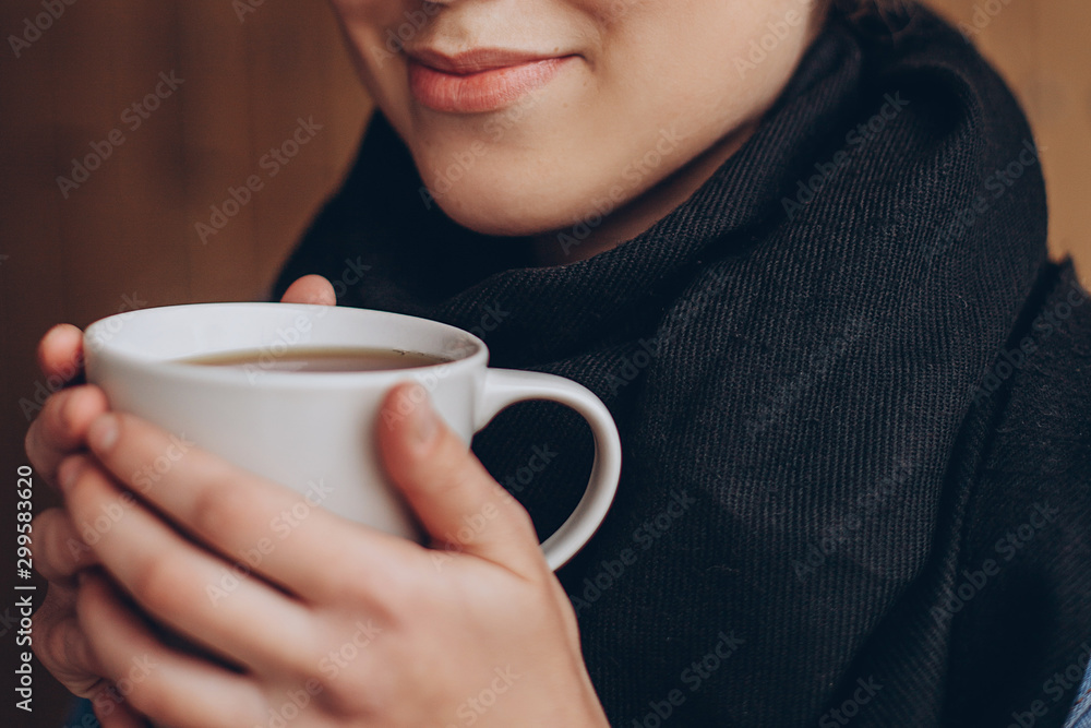 a mug of hot coffee or tea in the hands of a young pretty girl near her lips. Cropped photo with focus on cup a mug of hot coffee or tea in the hands of a young pretty girl near her lips. Cropped photo with focus on cup