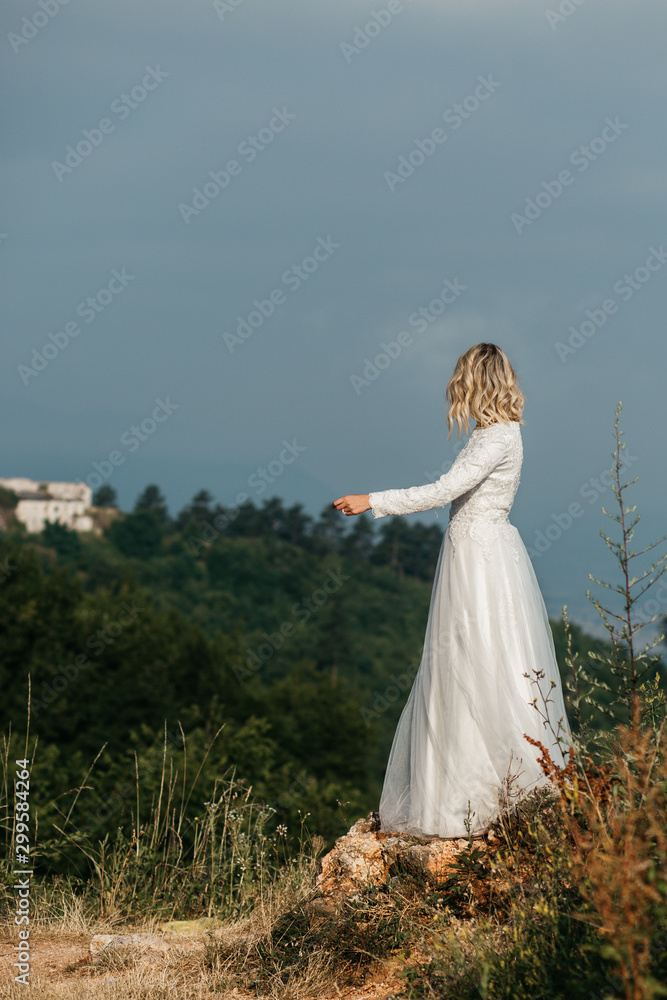 Beautiful elegant bride in lace wedding dress with long full skirt and long sleeves. Pretty girl in white. Nature, with city in the background.