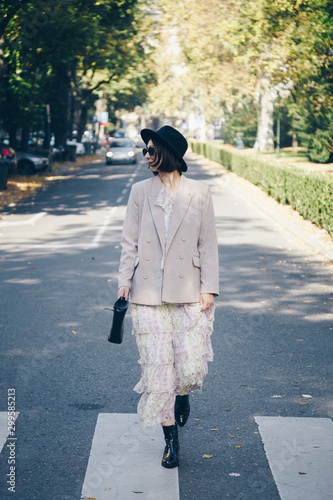 fashion blogger street style. fashionable woman posing wearing an oversized blazer, floral vintage dress, black ankle boots and a black trendy mini handbag. detail of a perfect fall 2019 outfit. 