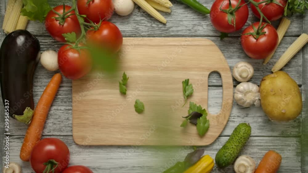 Parsley leaves falling on a cutting board in slow motion with organic vegetables around. Healthy vegetarian food concept. Nutritious products on a gray wooden table. Vertical camera shooting Parsley leaves falling on a cutting board in slow motion with organic vegetables around. Healthy vegetarian food concept. Nutritious products on a gray wooden table. Vertical camera shooting