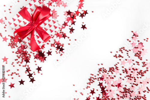 Christmas present with red bow on white background with red stars and sparkles. Xmas banner. Happy New Year. Flat lay style.