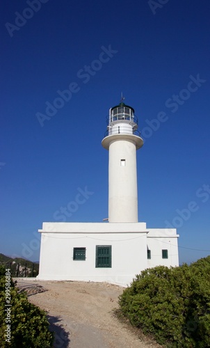 Old stone built lighthouse of Lefkada island south cape at summer, clear deep blue sky at background. A path through shrubs and bushes at the foreground