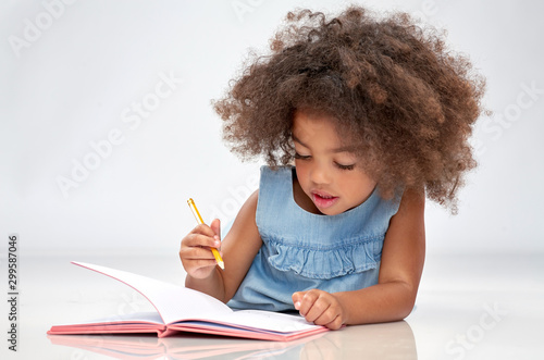 childhood, creativity, drawing and people concept - happy little african american girl with sketchbook and pencil over grey background photo