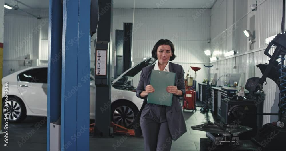Happy and charismatic lady worker at service auto walking in front of the camera thro the service auto very excited holding a map with a new signing contract Happy and charismatic lady worker at service auto walking in front of the camera thro the service auto very excited holding a map with a new signing contract