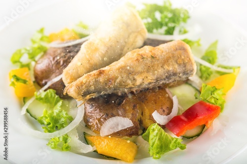 Fried fish in a salad on a white plate in the sun